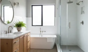 bathroom with wooden vanity, round mirror, potted fern, white freestanding tub with towel, and glass shower enclosure